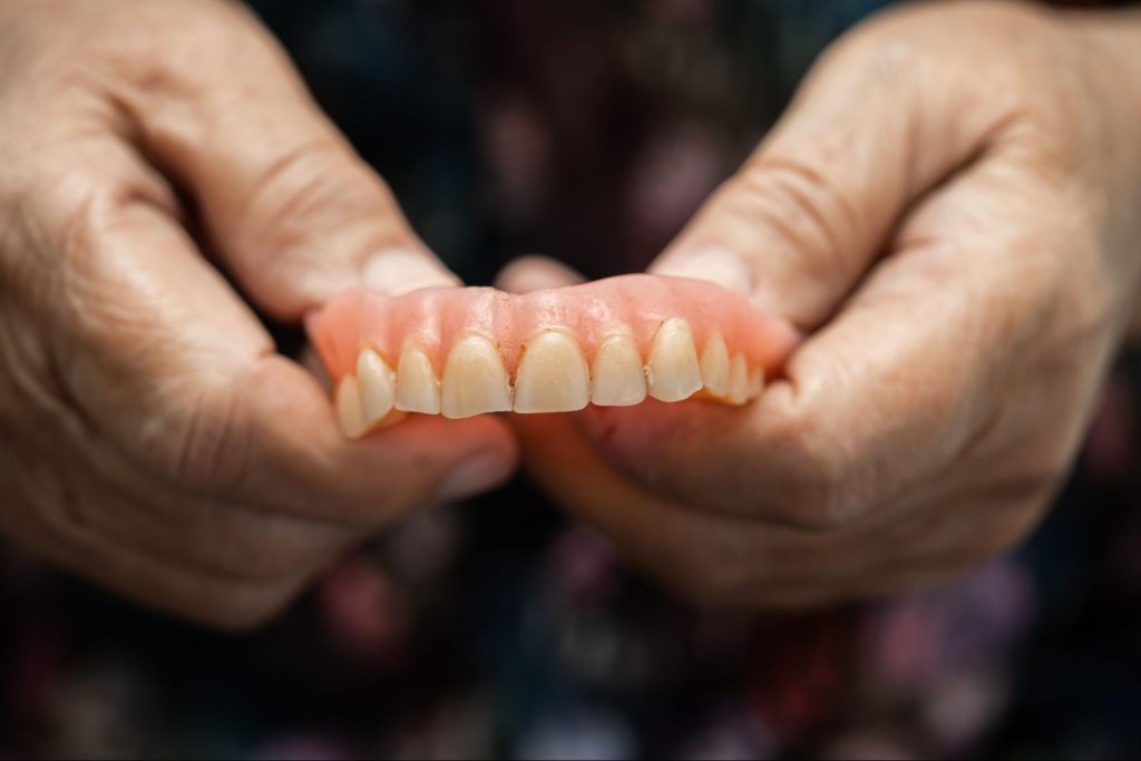 Elderly patient holding a worn upper denture showing flattened and discoloured teeth