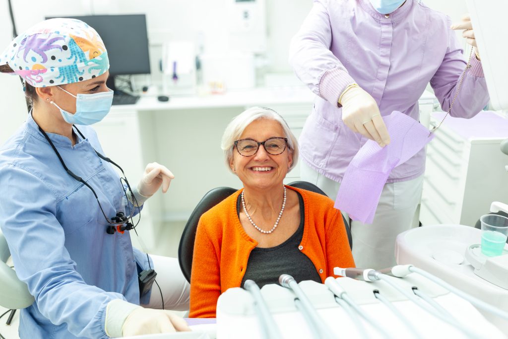 Senior woman smiling during a dental checkup, representing denture care, oral health, and insurance coverage